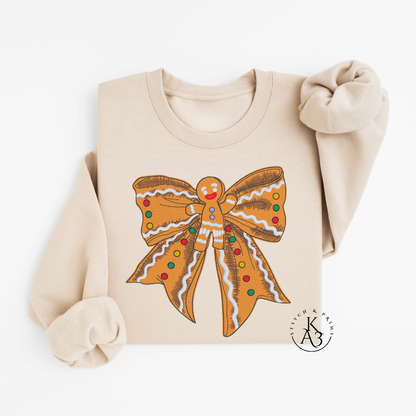 Beige sweatshirt with an embroidered gingerbread man bow design on a white background