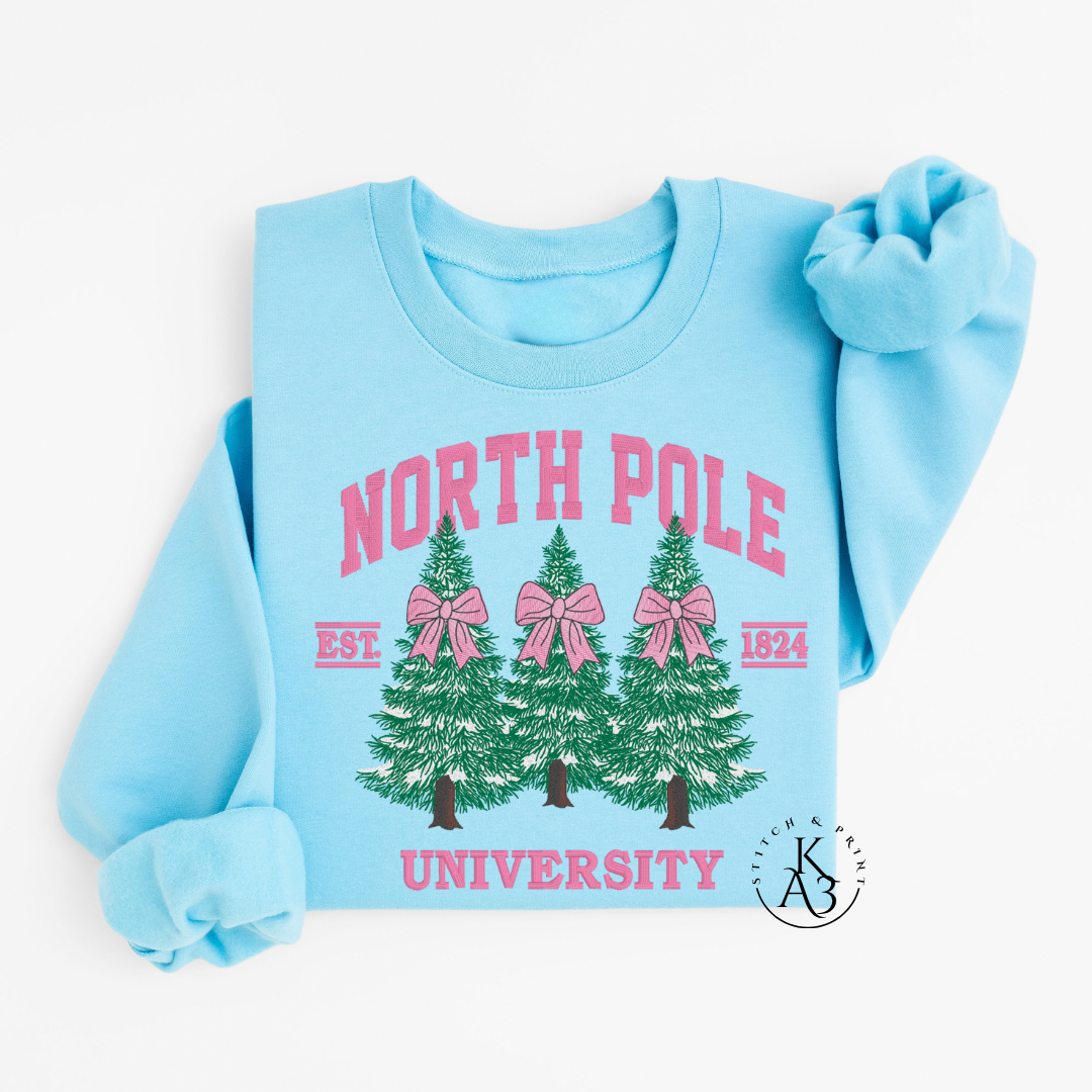 Light blue sweatshirt with embroidered 'North Pole University' text and Christmas tree design on a white background