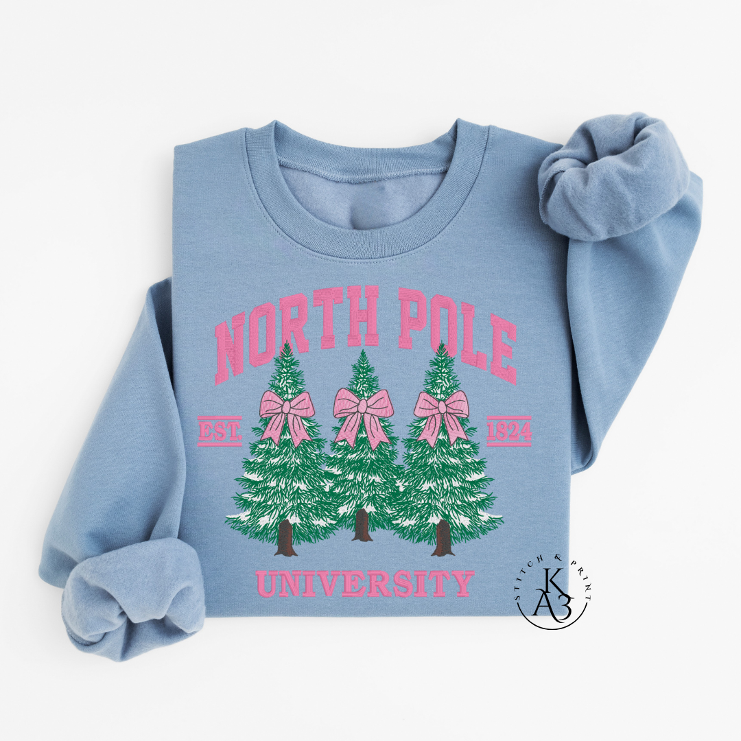 Light blue sweatshirt with embroidered 'North Pole University' text and Christmas tree design on a white background