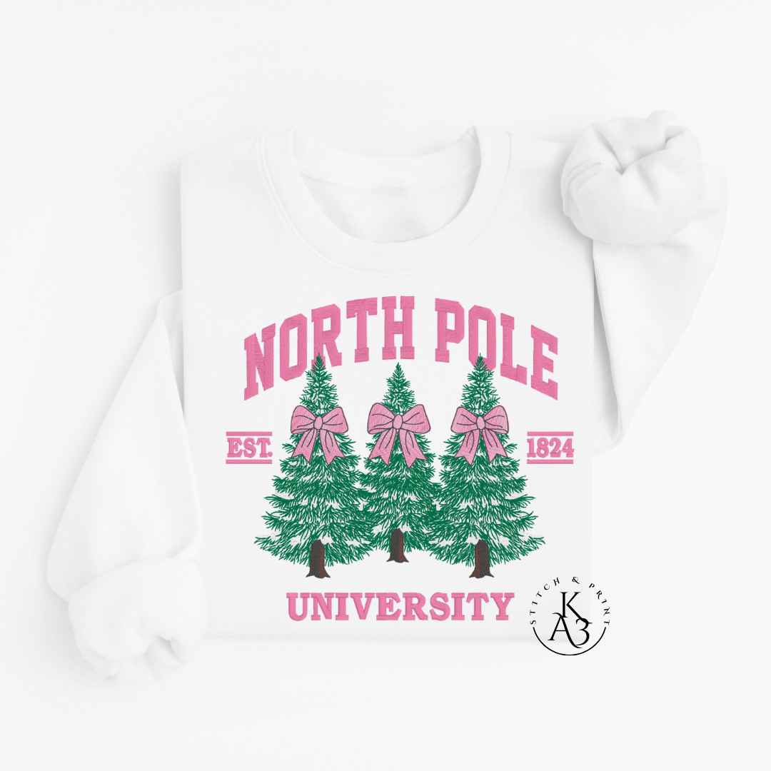 White Sweatshirt with embroidered green trees, pink bows, and 'North Pole University' text on a white background