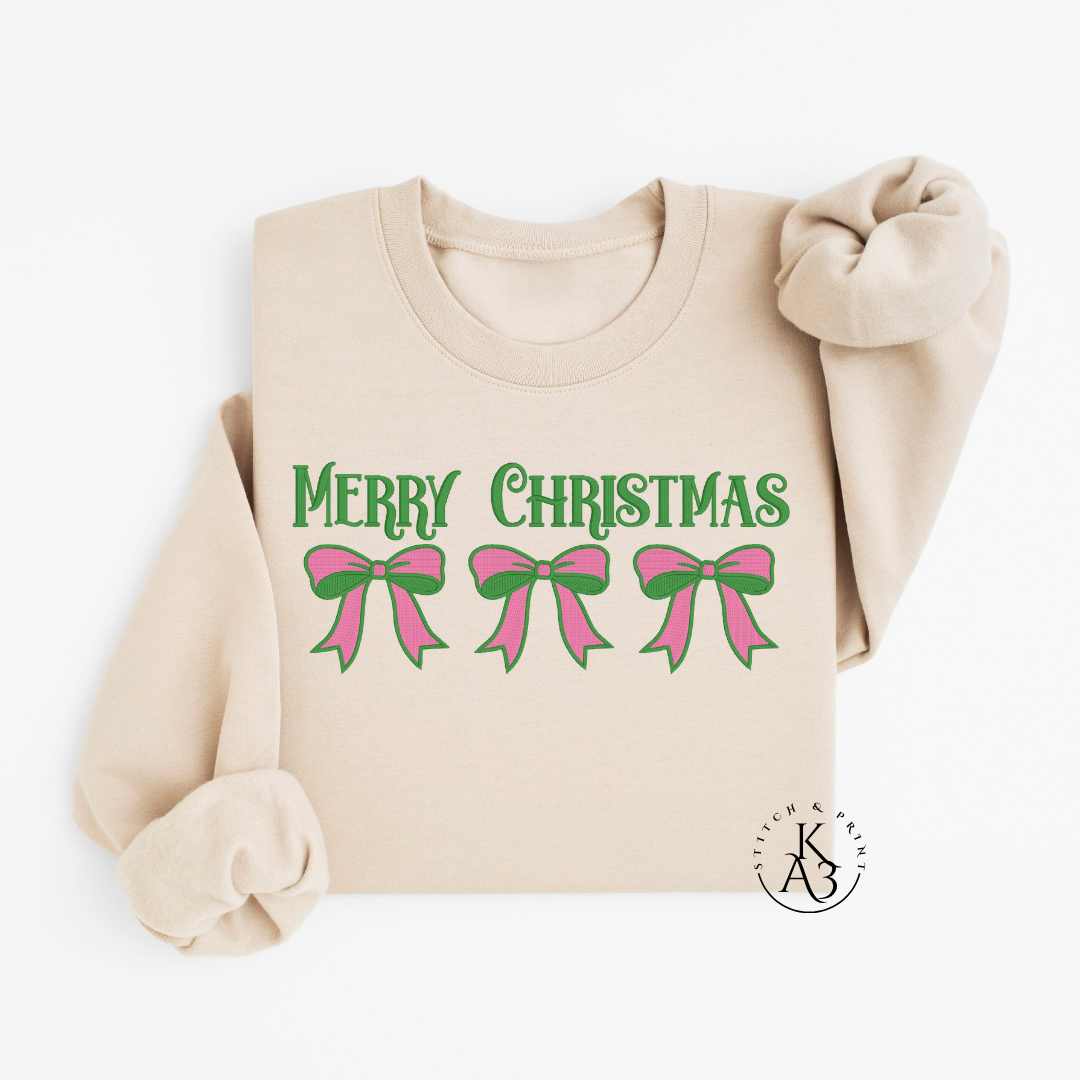 Beige sweatshirt with an embroidered 'Merry Christmas' text and pink bows on a white background